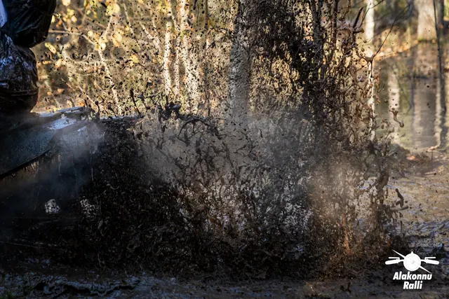 Alakonnu Rally 2026: a high spray of muddy water rises beside a motorcycle wheel in the flooded forest track.