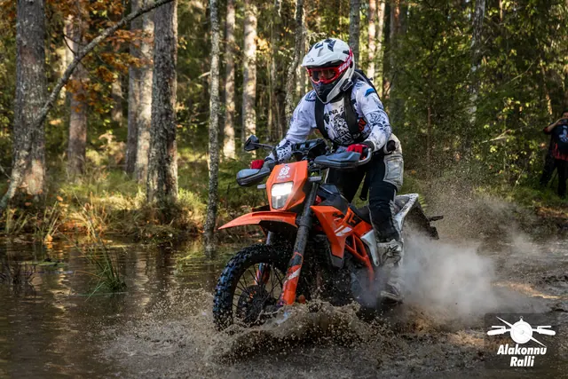 Alakonnu Ralli 2026: valge kiivriga sõitja paiskab oranžil mootorrattal metsaraja vett üles.