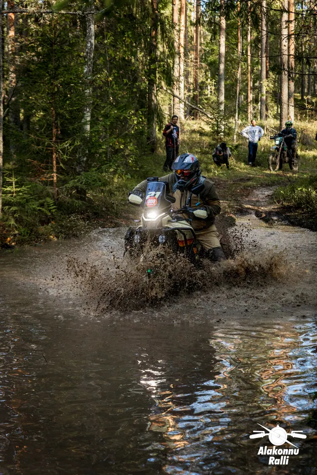 Alakonnu Ralli 2026: mootorrattur sõidab läbi metsaraja vee, pritsmed tõusevad esiratta ümber.