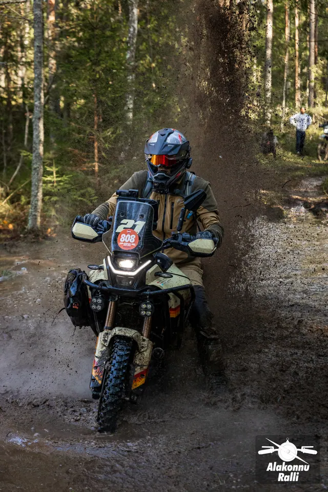 Alakonnu Ralli 2026: tumedas sõiduvarustuses osaleja läheneb mööda mudast metsarada, tagaratta taga pritsib vesi.
