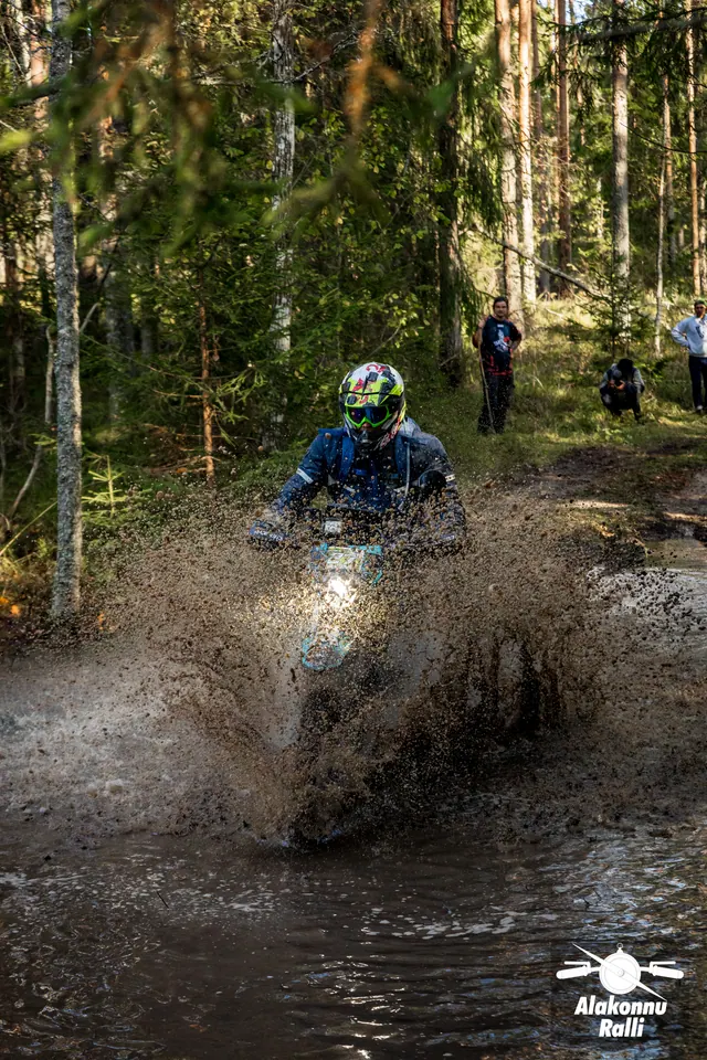 Alakonnu Ralli 2026: mootorrattur läheneb läbi metsaraja veetakistuse suure mudase pritsmepilvega.
