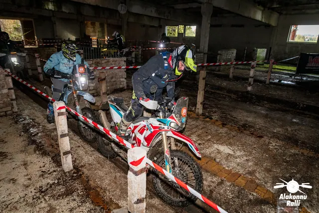Alakonnu Ralli 2026: sõitja juhib punast ja valget mootorratast hoones rajalintide vahel, teised ratturid taga.