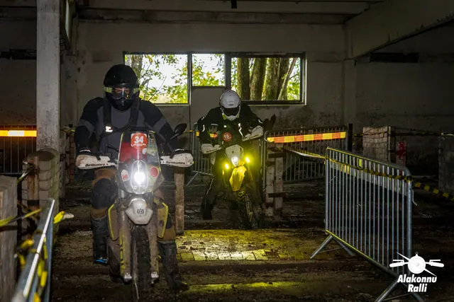 Alakonnu Ralli 2026: kaks mootorratturit läheneb hoones kitsas koridoris, esitulesid raamivad rajapiirded.