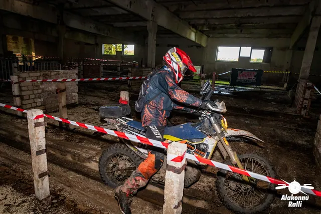 Alakonnu Ralli 2026: punase kiivriga sõitja juhib valget ja kollast mootorratast hoones mööda kitsast rada.