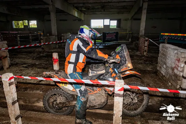 Alakonnu Ralli 2026: oranži ja musta sõidusärgiga osaleja juhib oranži mootorratast hoones lindiga piiratud rajal.