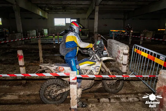 Alakonnu Ralli 2026: sinises ja kollases sõiduvarustuses osaleja juhib valget mootorratast hoones müüri kõrval.