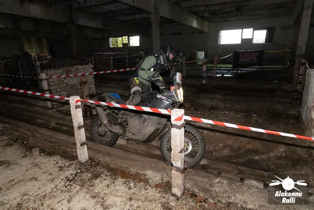 Alakonnu Ralli 2026: roheliste varrukatega sõitja juhib tumedat mootorratast hoones madalate müüride vahel.