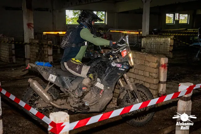 Alakonnu Ralli 2026: roheliste varrukatega sõitja pöörab tumeda mootorrattaga hoones tellismüüri kõrval.