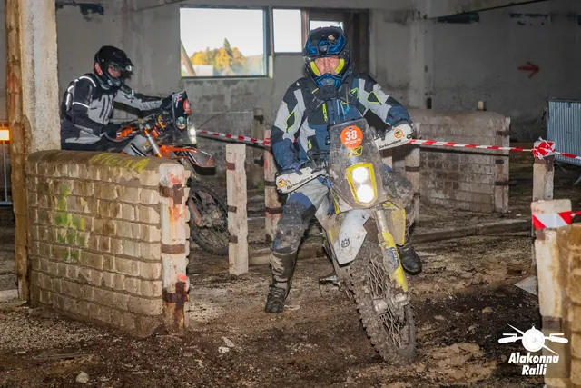 Alakonnu Ralli 2026: kaks mootorratturit läheneb hoones madala tellismüüri tagant, esimese ratta esituli põleb.