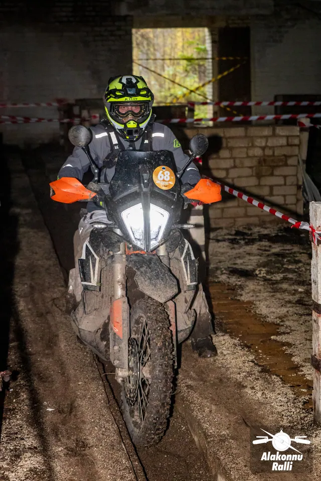 Alakonnu Ralli 2026: kollase ja musta kiivriga osaleja läheneb hoone kitsas rajakoridoris põleva esitulega.