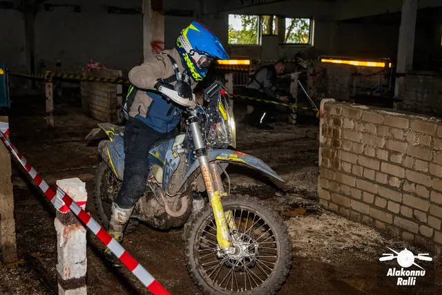 Alakonnu Ralli 2026: sinise ja kollase kiivriga sõitja pöörab valge mootorrattaga hoones tellismüüri kõrval.