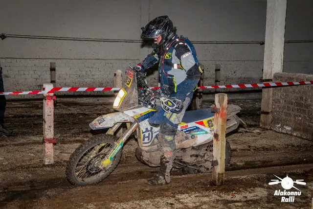 Alakonnu Ralli 2026: tumedas sõiduvarustuses osaleja pöörab valgel mootorrattal hoones rajalintide vahel.