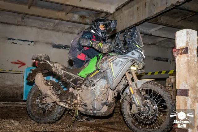 Alakonnu Ralli 2026: roheliste pükstega sõitja juhib porist mootorratast hoones kitsas müüridevahelises koridoris.