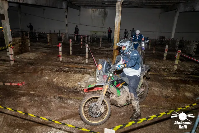 Alakonnu Ralli 2026: sinises ja hallis sõiduvarustuses osaleja läheneb hoones mootorrattal põleva esitulega.