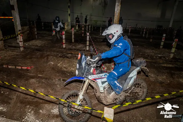 Alakonnu Ralli 2026: sinises sõiduvarustuses ja valge kiivriga osaleja juhib valget ja sinist mootorratast hoones.