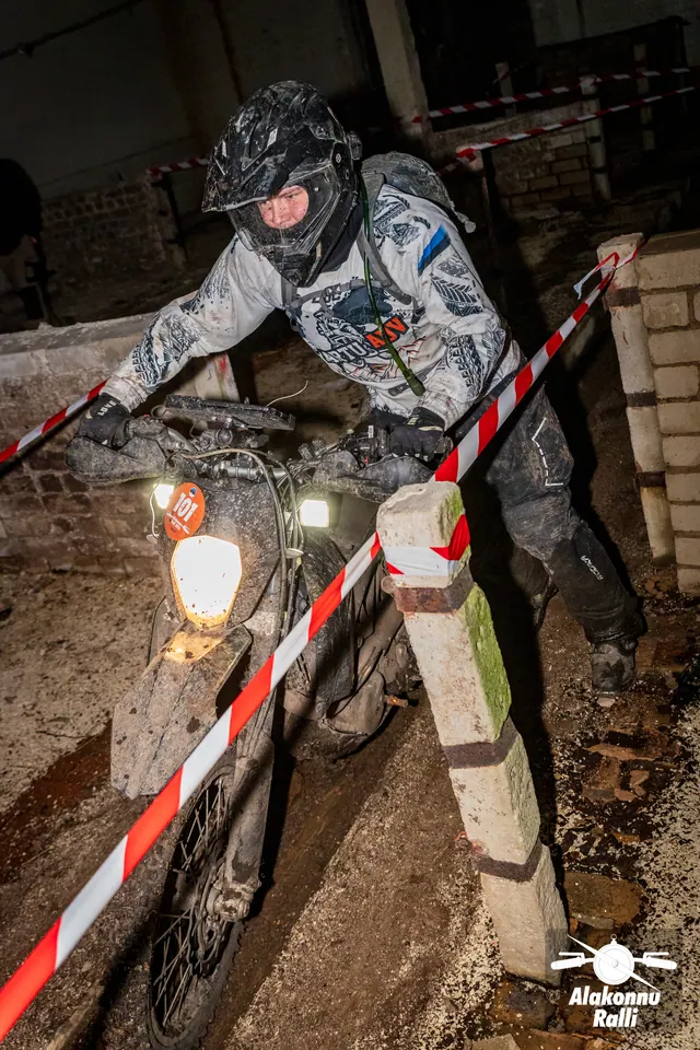 Alakonnu Ralli 2026: mootorrattur läheneb hoones kitsas rajakoridoris, esiratas punavalge rajalindi kõrval.