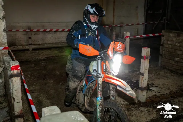 Alakonnu Ralli 2026: sõitja juhib oranžide käekaitsmetega mootorratast hoones kitsas müüridevahelises koridoris.