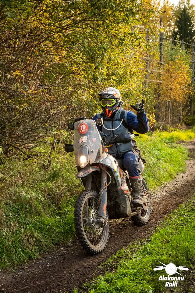 Alakonnu Ralli 2026: kollase ja musta kiivriga sõitja lehvitab mootorrattalt sügiseste puude kõrval kulgeval rajal.
