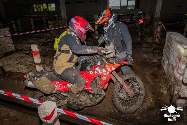 Alakonnu Ralli 2026: kaks kiivriga osalejat aitavad punast mootorratast hoones kitsas rajakoridoris.
