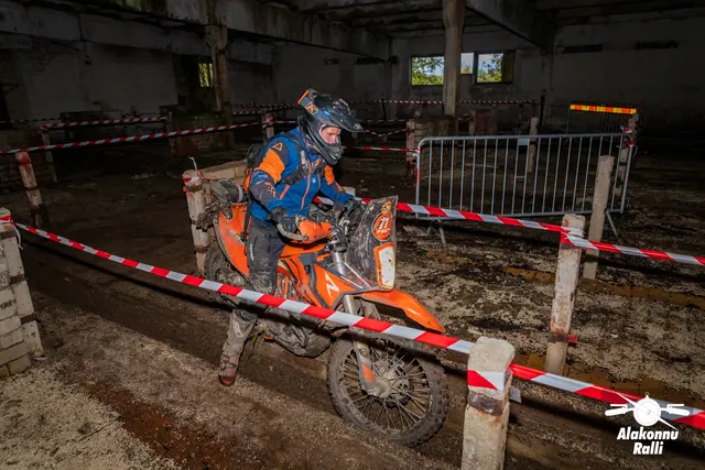 Alakonnu Ralli 2026: sinises ja oranžis sõiduvarustuses osaleja juhib oranži mootorratast hoones rajalindi kõrval.
