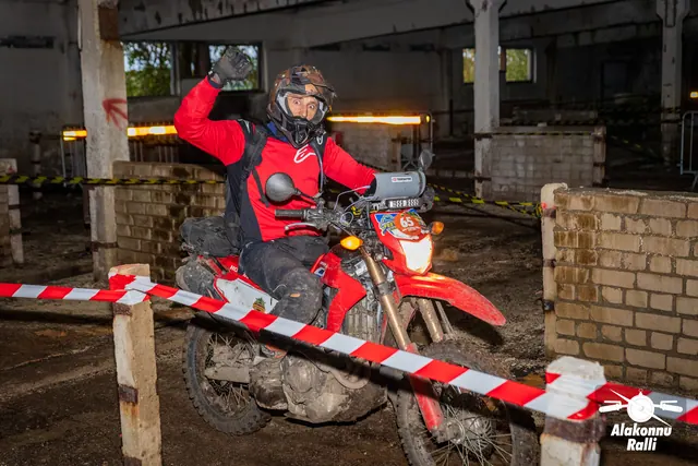 Alakonnu Ralli 2026: punases sõiduvarustuses osaleja lehvitab oranžilt mootorrattalt hoone rajakoridoris.