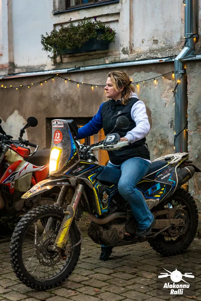 Alakonnu Ralli 2026: ilma kiivrita inimene istub hoone seina ääres porisel mootorrattal, taustal valguskett.