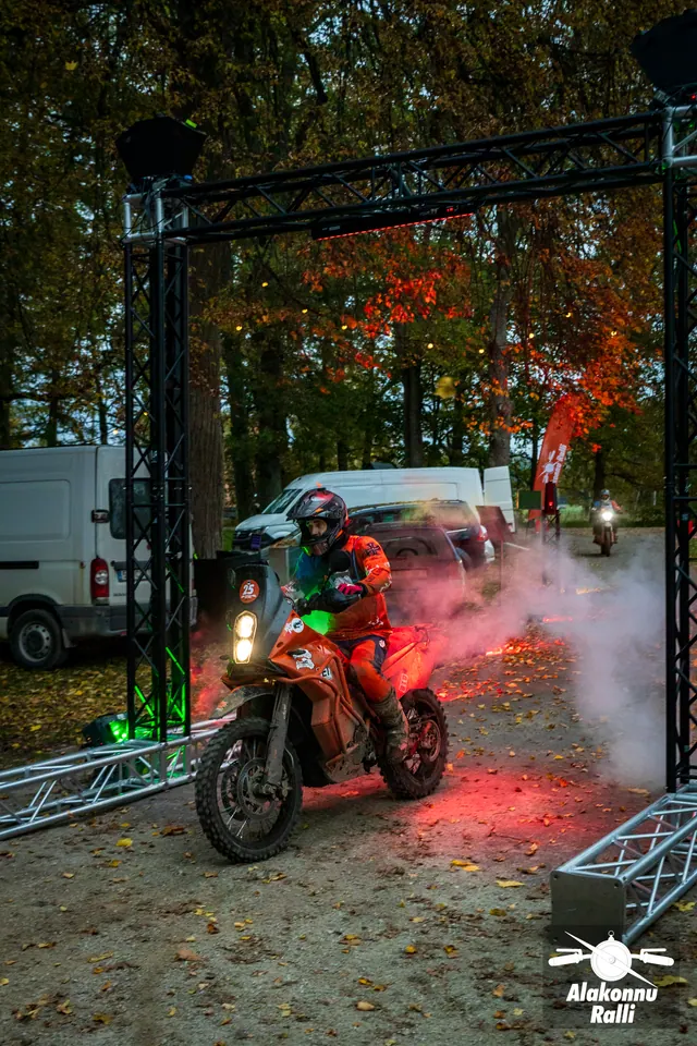 Alakonnu Ralli 2026: mootorrattur sõidab õues läbi metallraami, ümber punane valgus ja hele suits.