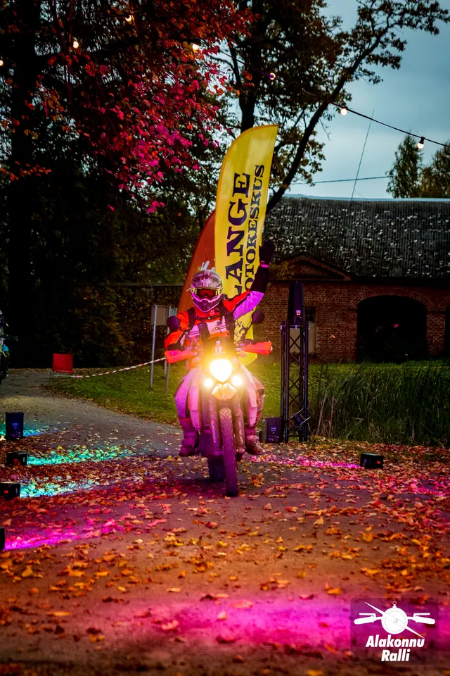 Alakonnu Ralli 2026: mootorrattur läheneb õues põleva esitulega, ümber roosa valgus ja sügisesed lehed.