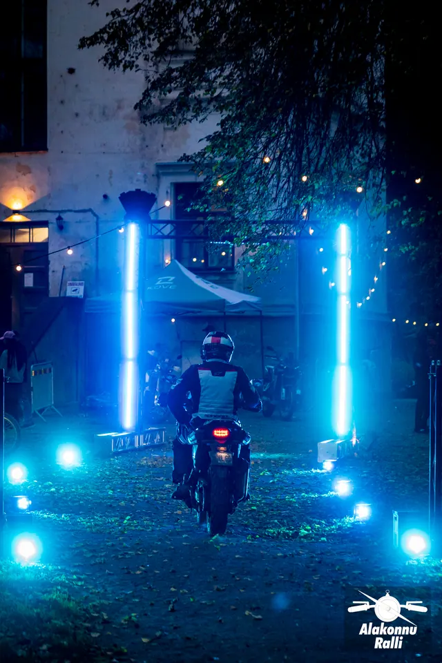Alakonnu Ralli 2026: mootorrattur sõidab hämaras õues läbi siniste valgusribadega metallraami.