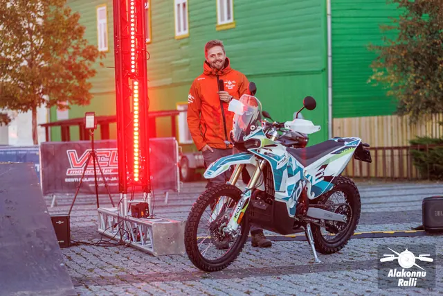 An organizer beneath the start gate beside a motorcycle – Alakonnu Rally 2026, start and SS1