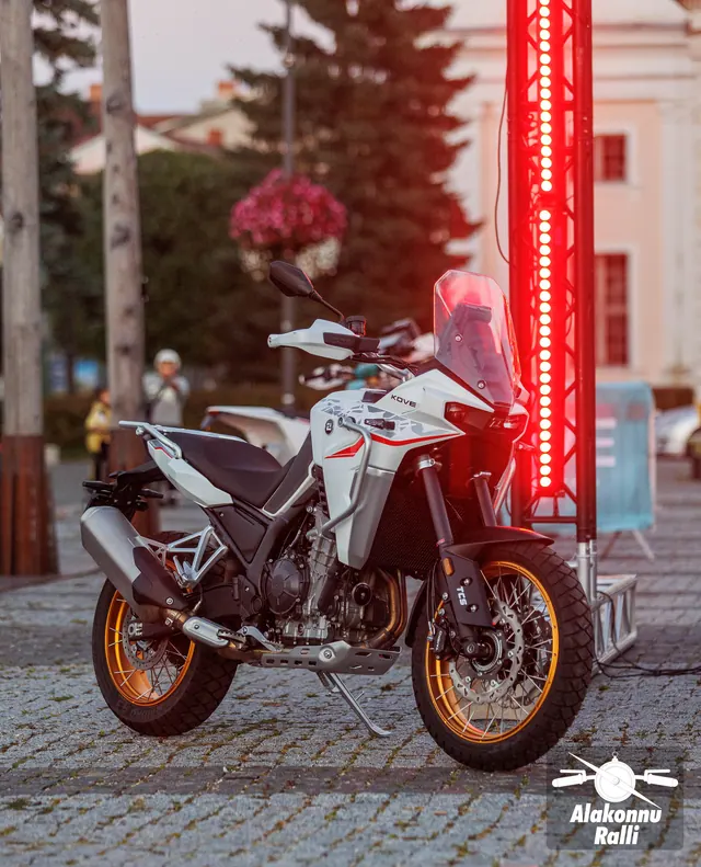Motorcycle riders beneath the start gate at the evening rally start – Alakonnu Rally 2026, SS1